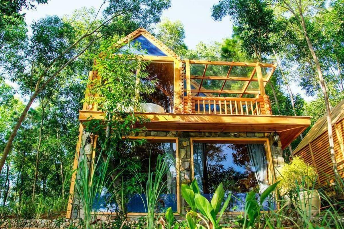 A wooden treehouse with a balcony, surrounded by lush greenery.
