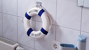 Ein Badezimmer mit Handtuchhalter, gefalteten Handtüchern, einem Rettungsring mit der Aufschrift 'WELCOME ON BOARD' und einem weißen Heizkörper.