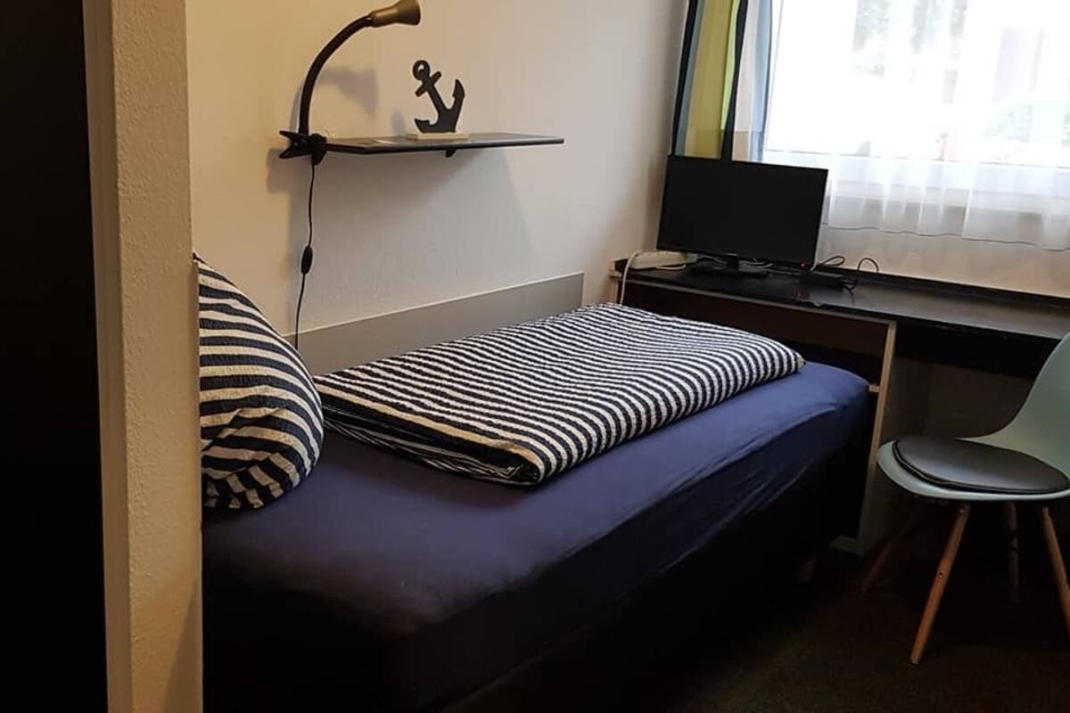 A small room with a bed, a desk, a chair, and a shelf with a decorative item.
