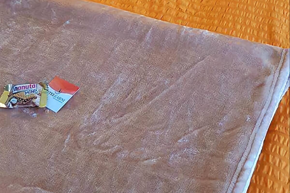 A neatly made bed with an orange blanket and pillow, a small table with a lamp and a cup, and a sign indicating no smoking.