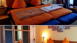 Ein Hotelzimmer mit Bett, orangefarbener Bettwäsche, einem Nachttisch mit Lampe und Bildern an den Wänden.