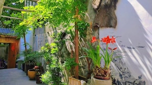 Un patio tradicional con plantas en macetas, una estructura de madera y un mural en la pared.