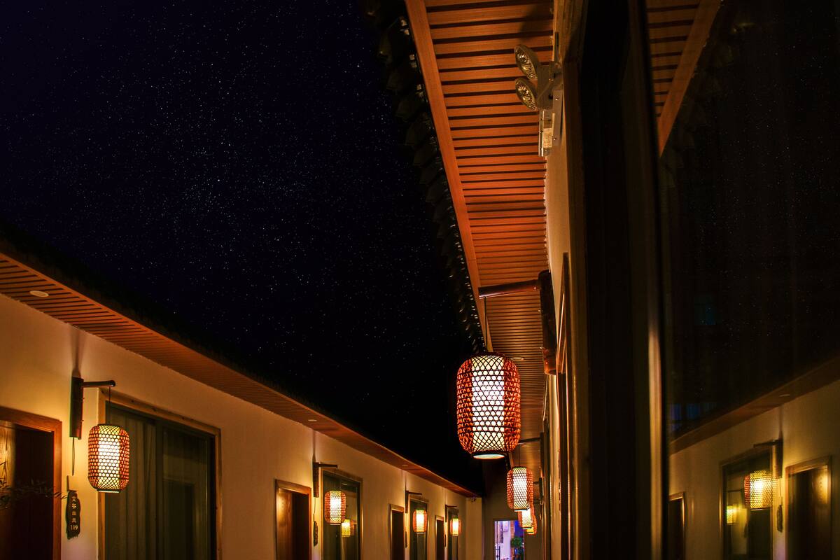 Pasillo de hotel con varias puertas, cielo nocturno estrellado y faroles colgantes.