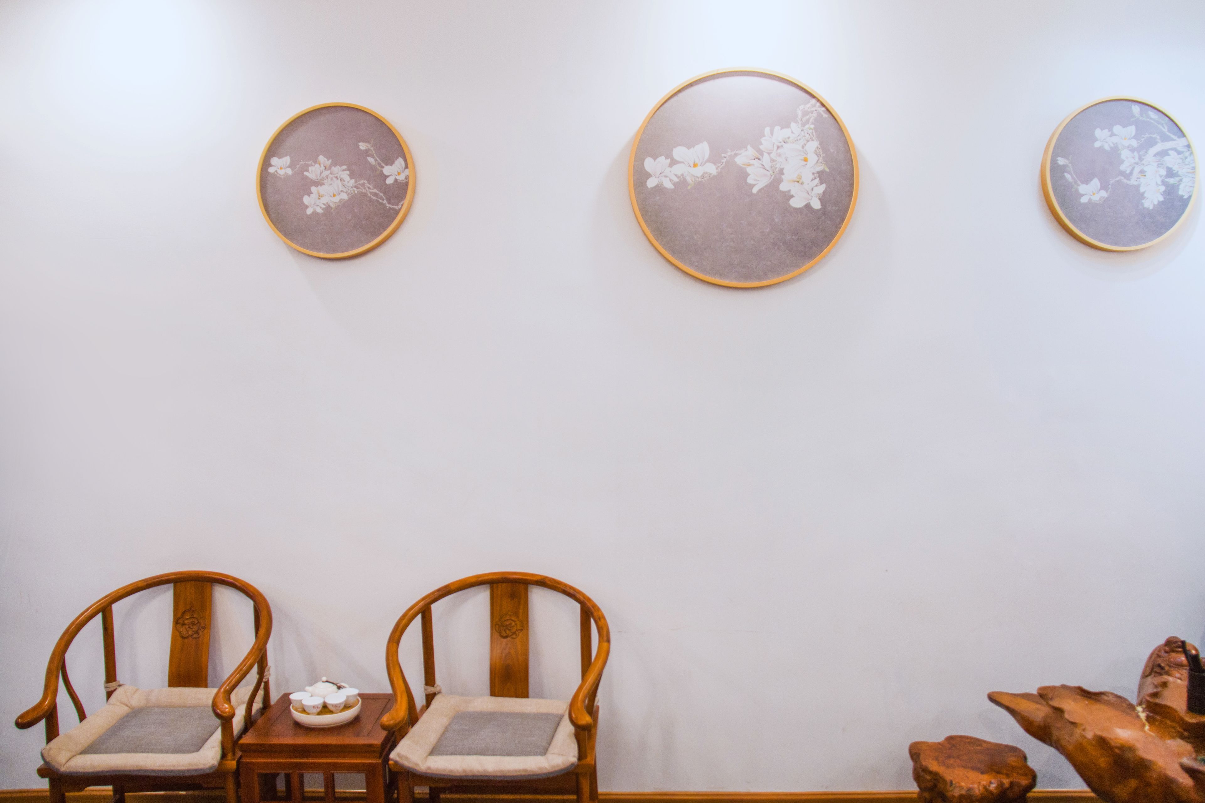 A room with two wooden chairs and a small table with a bowl of cookies. There are three framed artworks on the wall.