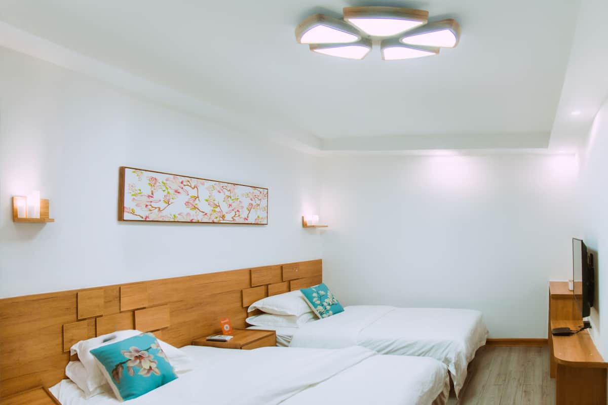 Habitación de hotel con dos camas, cabecera de madera, televisor montado en la pared y lámpara en el techo.