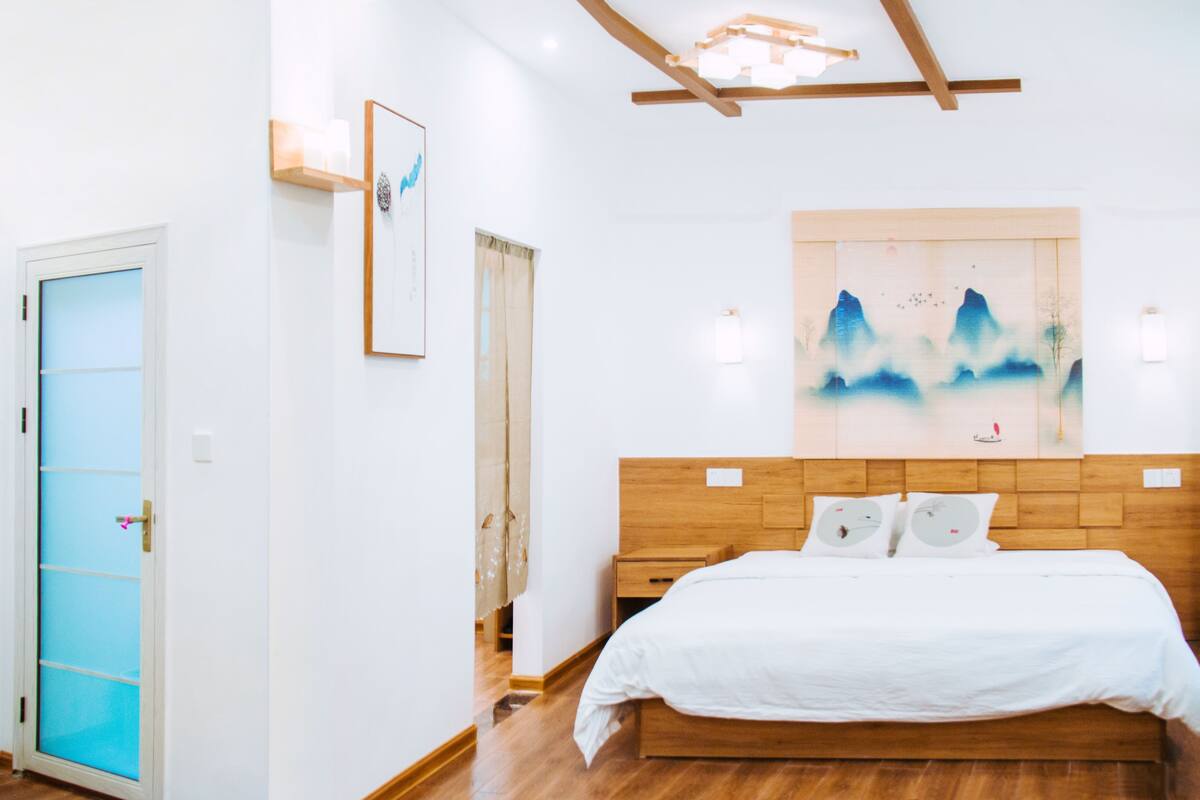 Un dormitorio con una cama de madera, un cuadro grande en la pared y una ventana con cortinas.