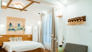 Habitación de hotel con una cama de madera, un sofá gris, una mesita con un florero y un perchero en la pared.