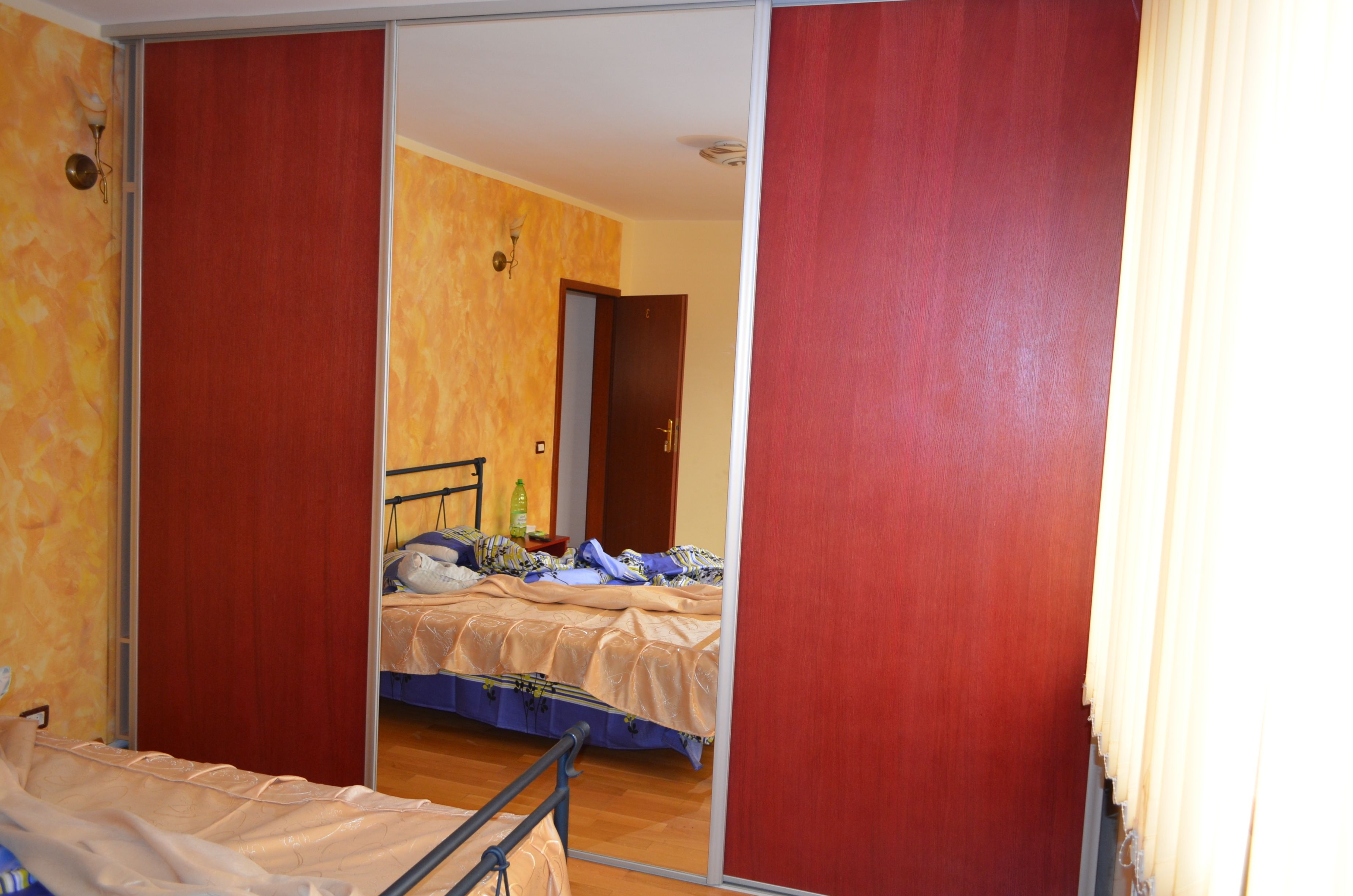 Una habitación con una cama, un espejo y suelo de madera.