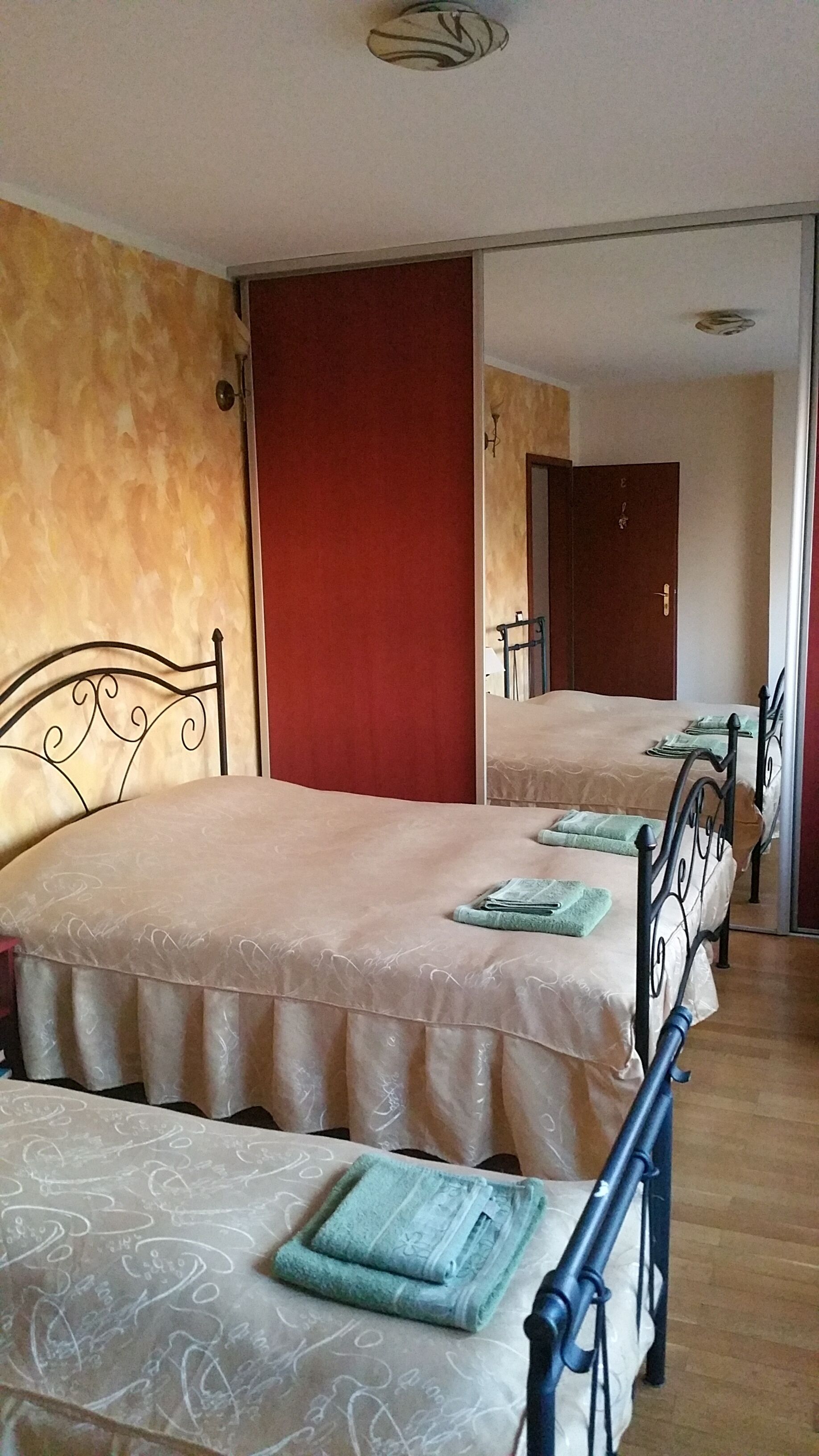 A hotel room with two beds, a red wall, and a wooden floor.