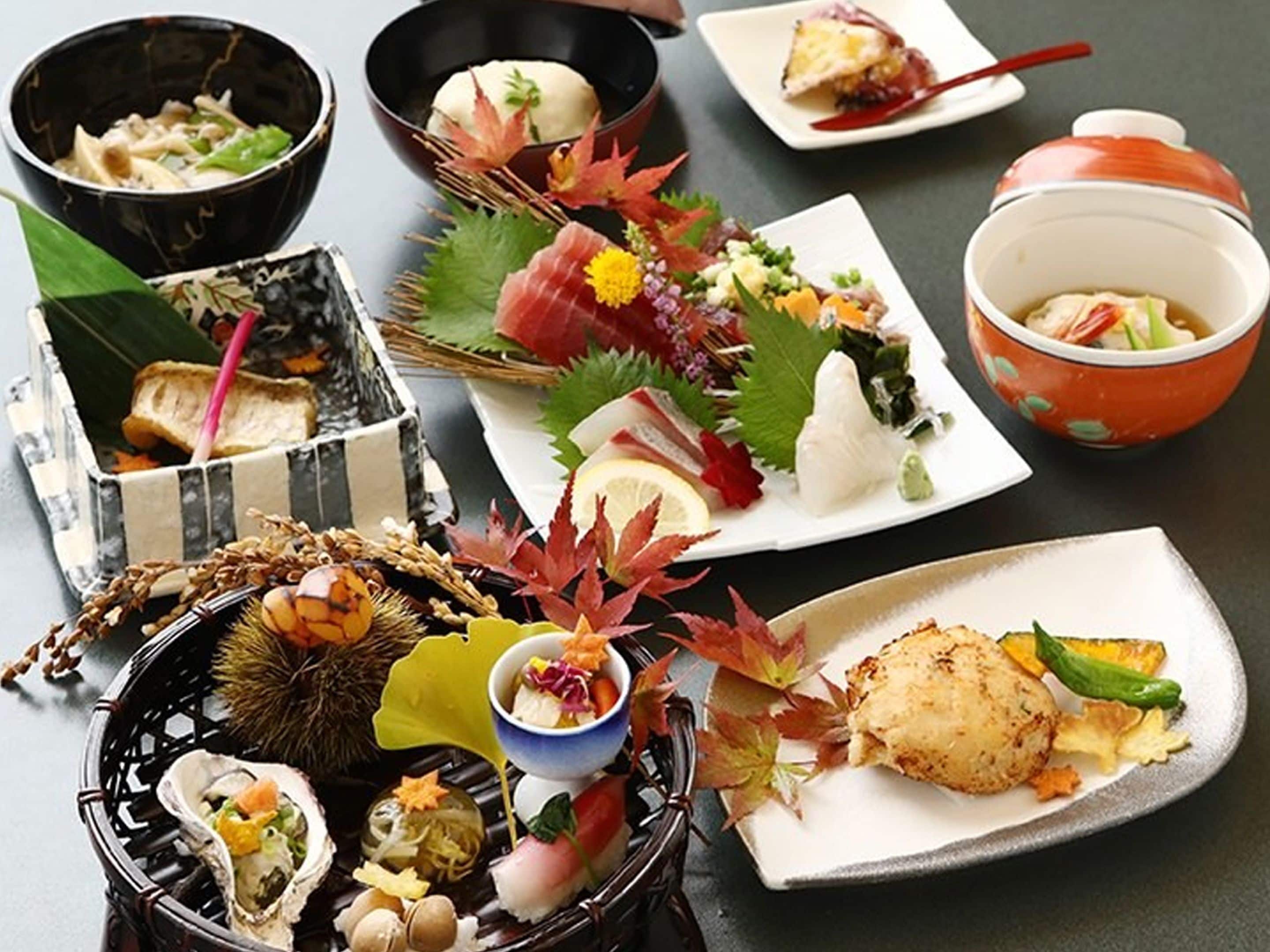A variety of Japanese dishes, including sushi and sashimi, arranged on a table with different types of bowls and plates.