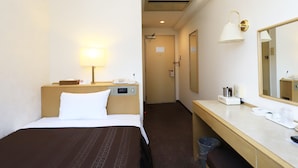 A hotel room with a bed, bedside table, lamp, mirror, and a desk with a trash bin. - Kawagoe Dai-Ichi Hotel (Kawagoe)