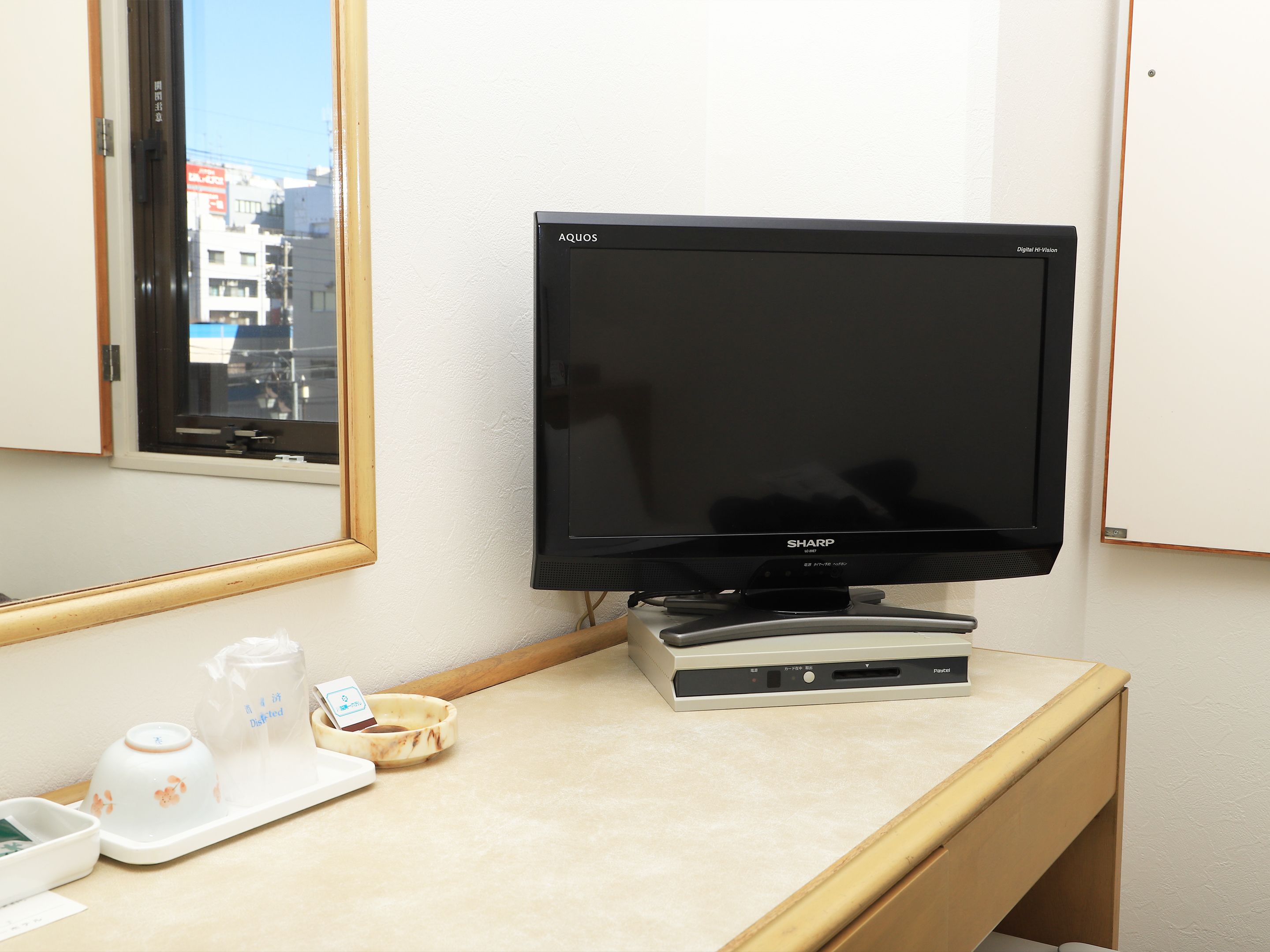 A hotel room with a television, a small table with a tray, and a window with a view of buildings.