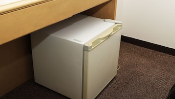 A compact, white refrigerator under a wooden counter in a room with a brown carpet.