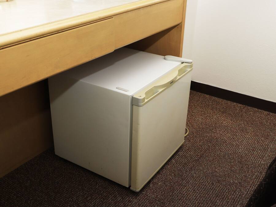 A compact, white refrigerator under a wooden counter in a room with a brown carpet.