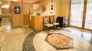 A reception area with a wooden counter, two chairs, a small table with a vase, and a tiled floor with a circular pattern. - Kawagoe Dai-Ichi Hotel (Kawagoe)