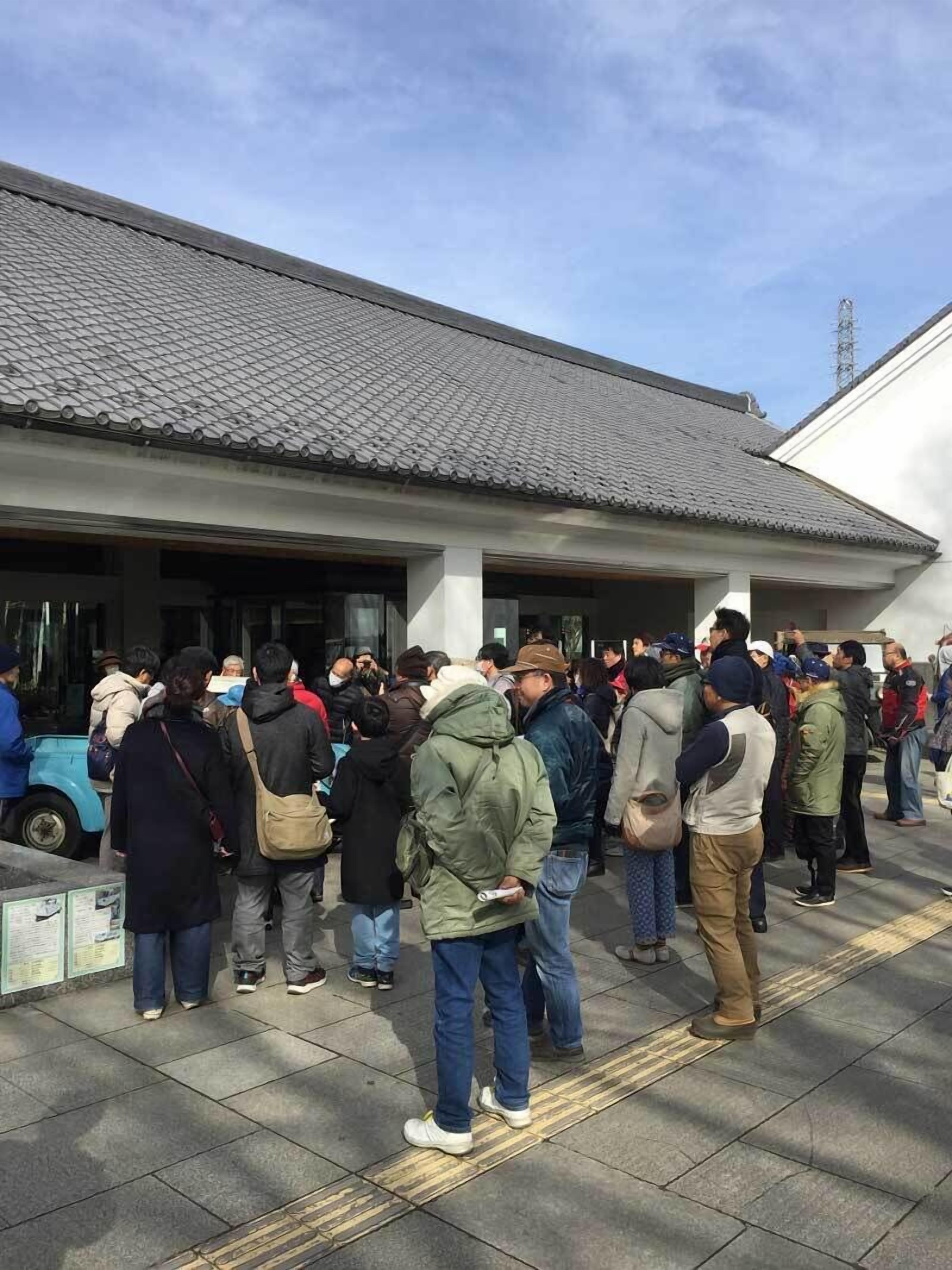 A group of people standing outside a building with a tiled roof and a white facade.