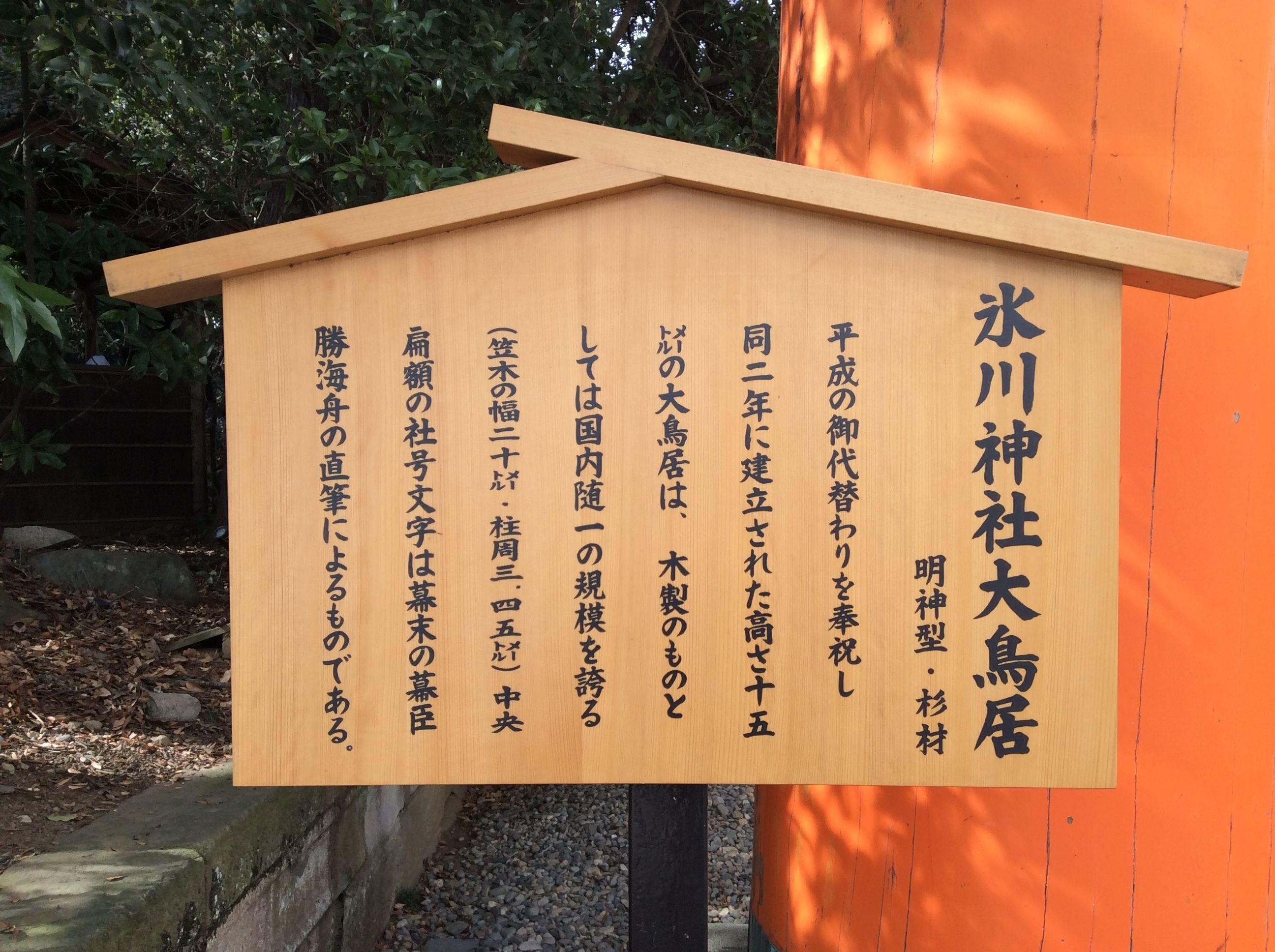 A wooden sign with Japanese text, mounted on a post with an orange background.