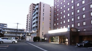 A multi-story hotel with a modern facade, a ground-level entrance, and a parking area with cars. - Kawagoe Dai-Ichi Hotel (Kawagoe)