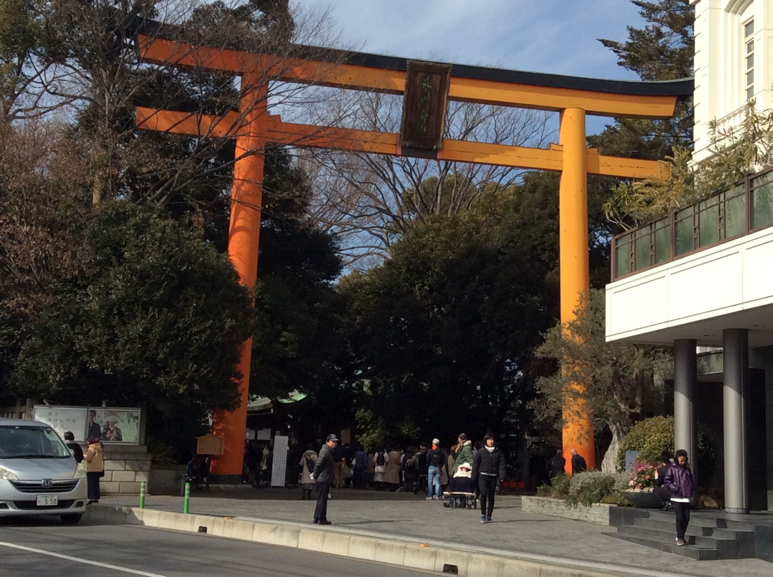 A traditional Japanese torii gate in an urban setting with modern buildings and pedestrians.
