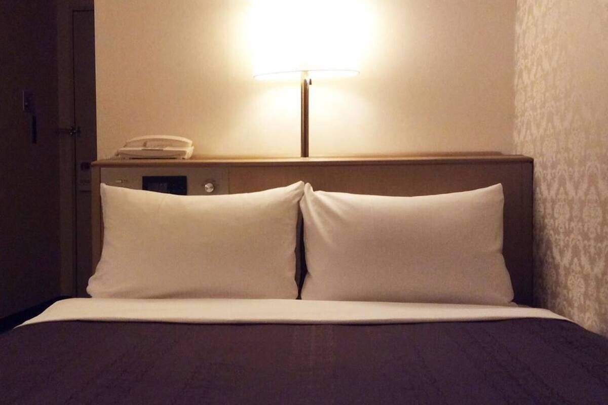 A hotel room with a bed, a nightstand with a lamp, and a telephone.