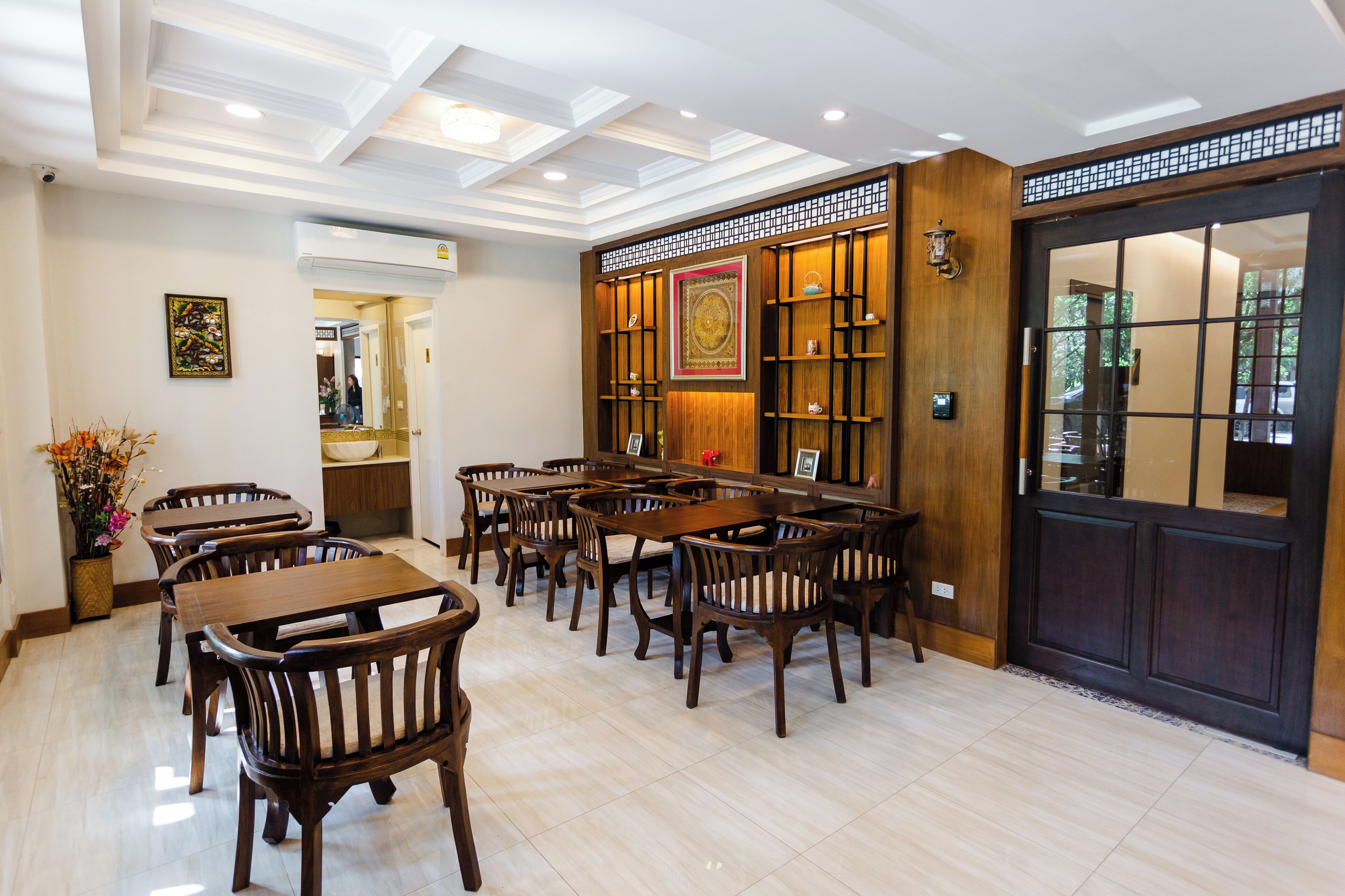 A dining area with wooden tables and chairs, a decorative wall with shelves, and a large wooden door with glass panels.