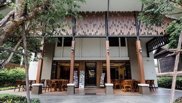 A modern building entrance with a covered patio area, wooden furniture, and a stone pathway. - Lima Lanna Hotel (Chiang Mai)
