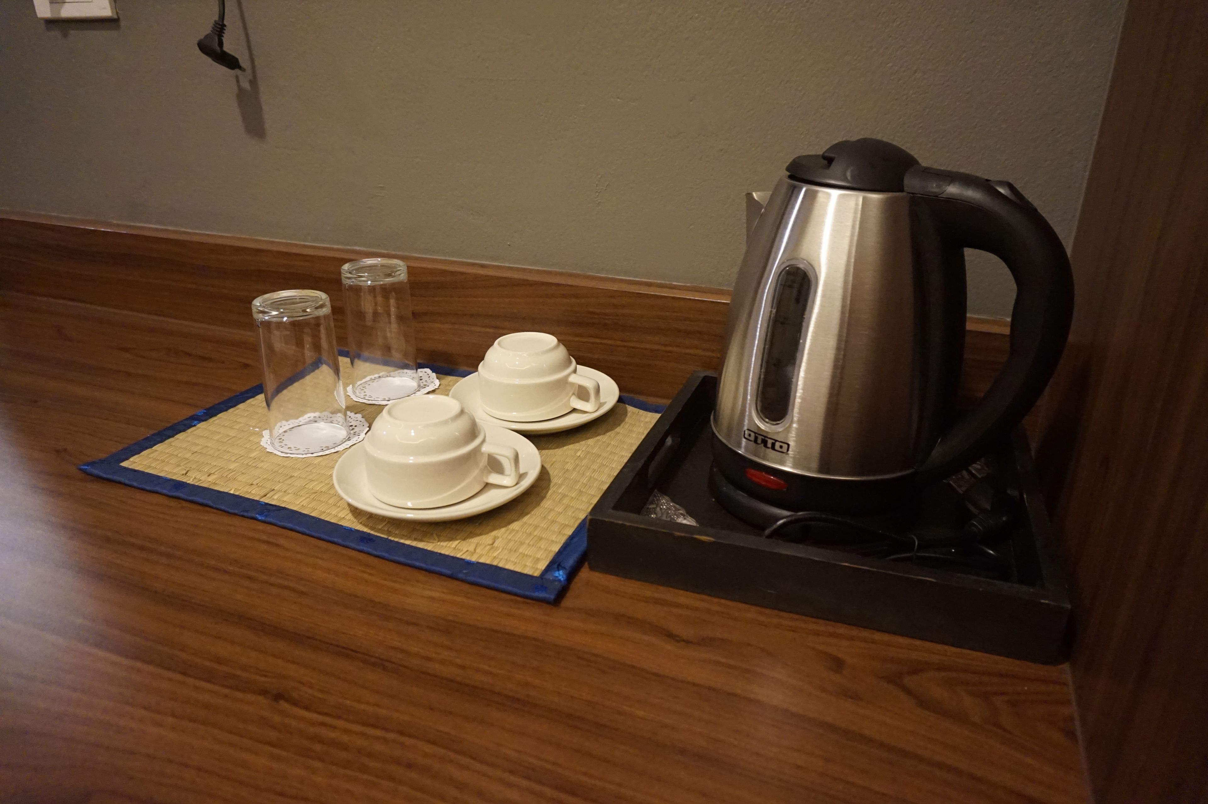 Una zona de cocina con un hervidor, dos tazas y dos vasos sobre un tapete.