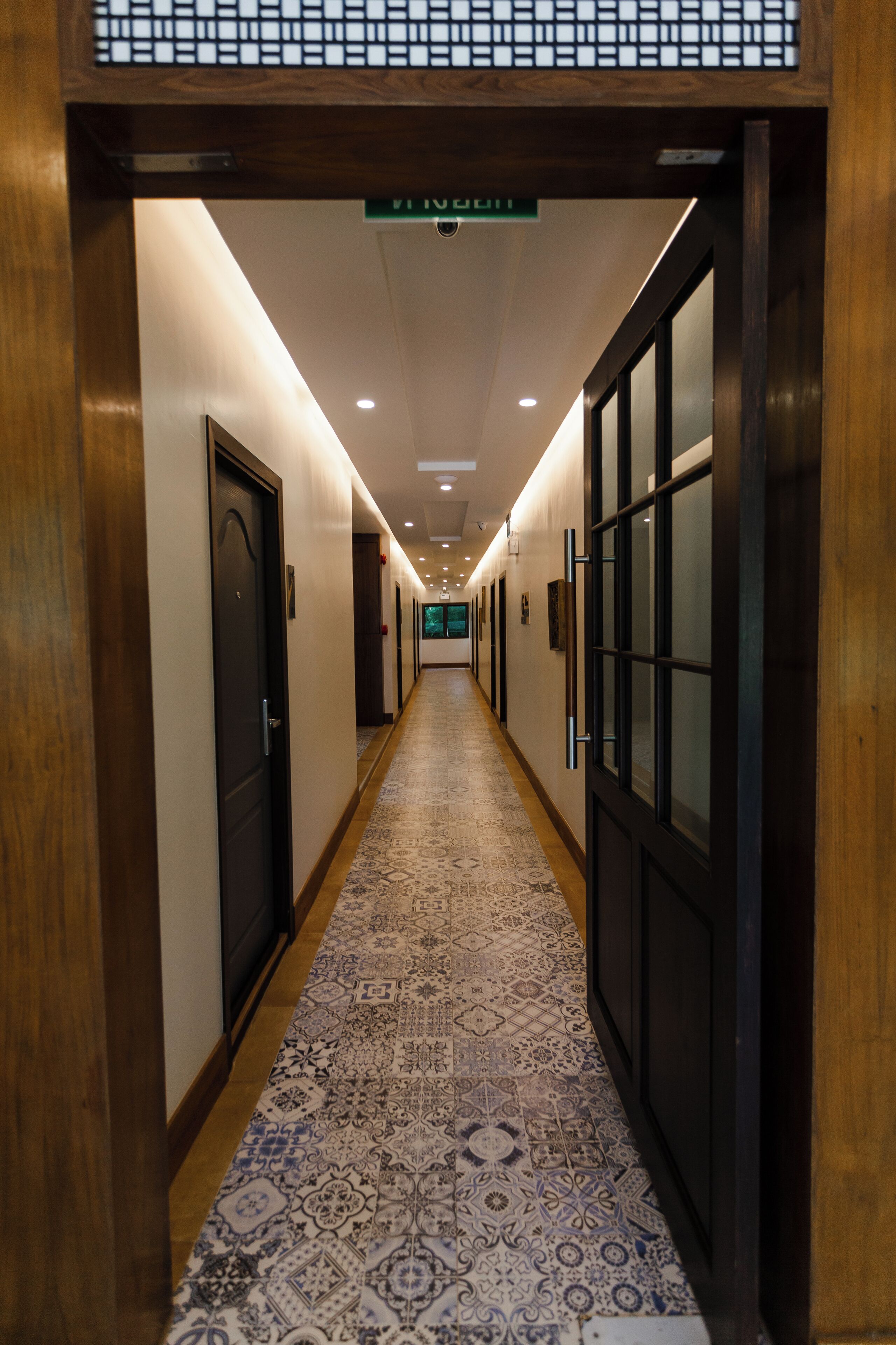 Un couloir d’hôtel avec un tapis à motifs, des murs en bois et des portes donnant accès aux chambres.