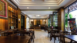 A spacious restaurant with wooden tables and chairs, a counter, and a view of greenery outside. - Lima Lanna Hotel (Chiang Mai)