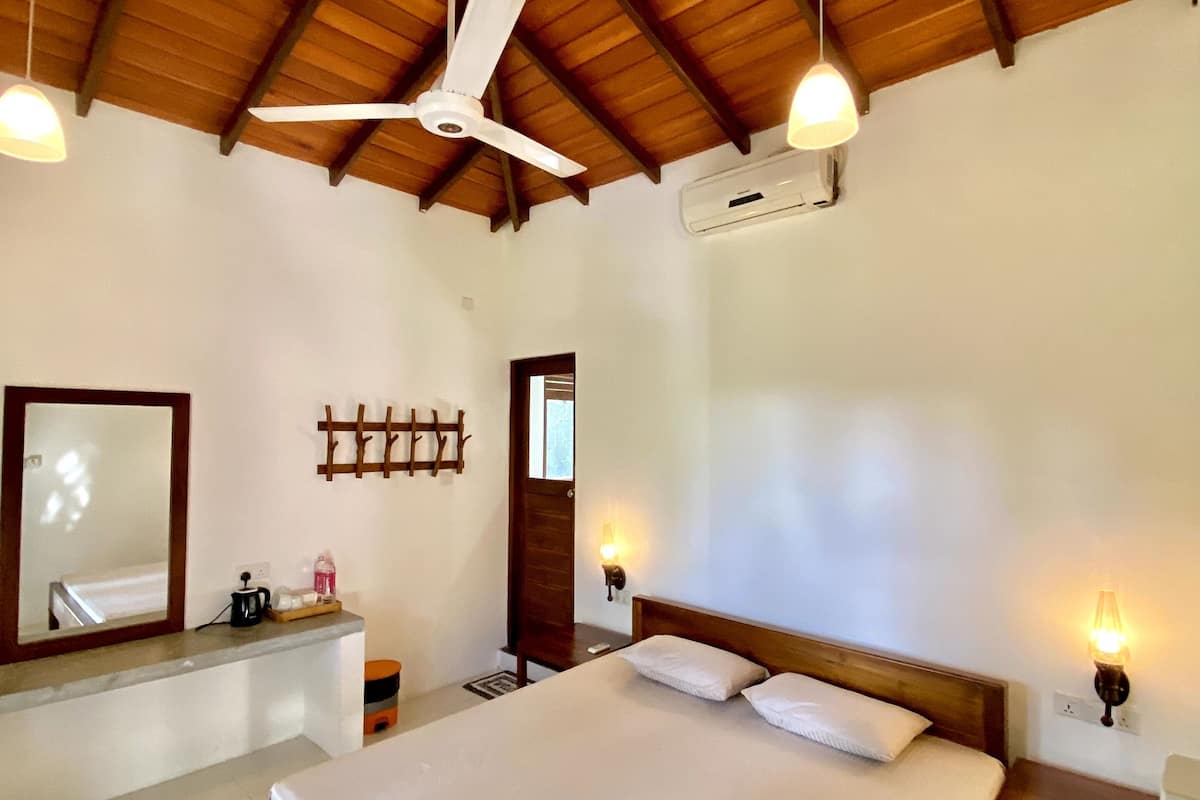 A spacious bedroom with a large bed, wooden ceiling beams, a ceiling fan, and a wall-mounted air conditioning unit.
