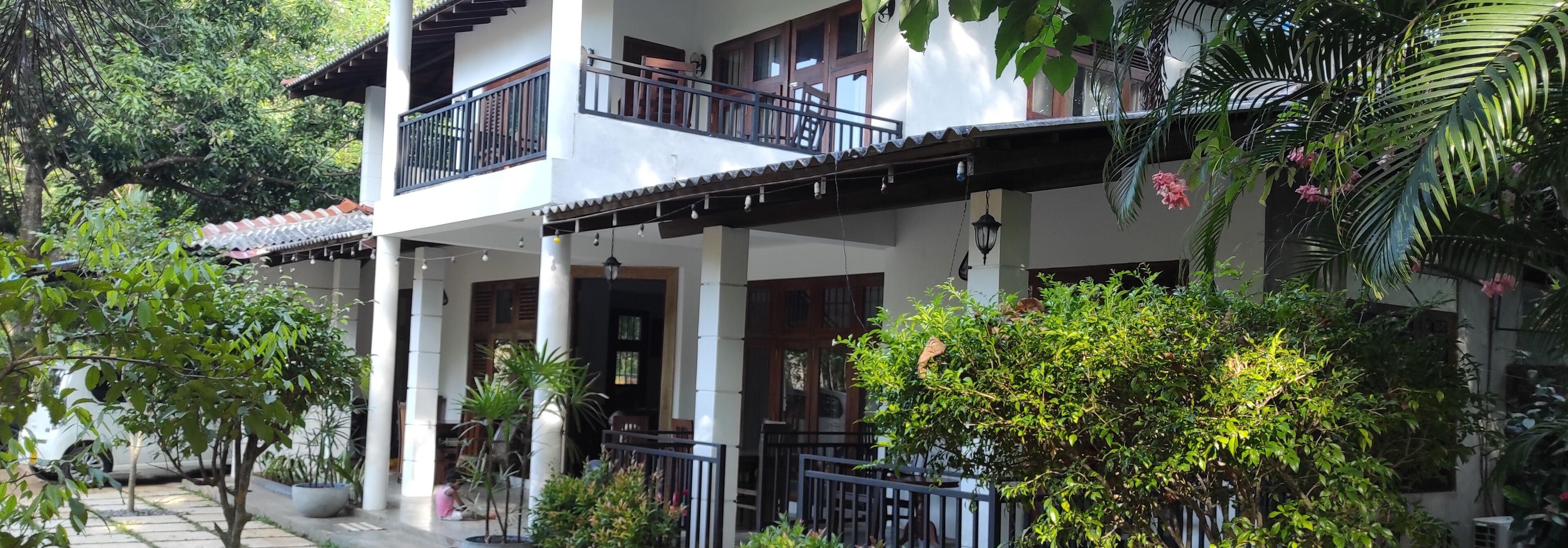 A two-story building with a balcony, columns, and potted plants.