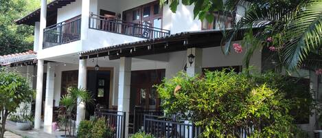 A two-story building with a balcony, columns, and potted plants.