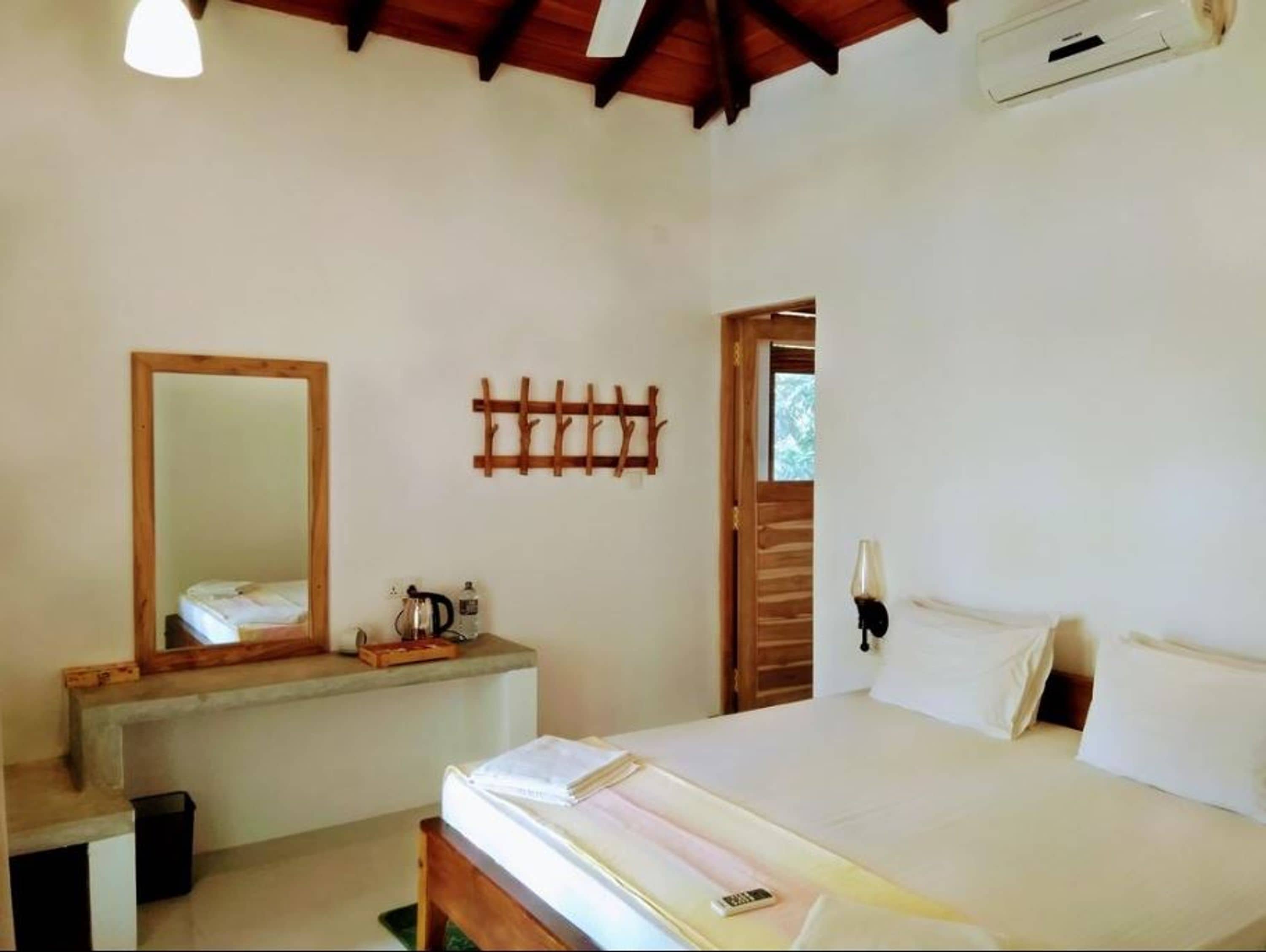 A bedroom with a bed, a bedside table, a mirror, and a wall-mounted light fixture.