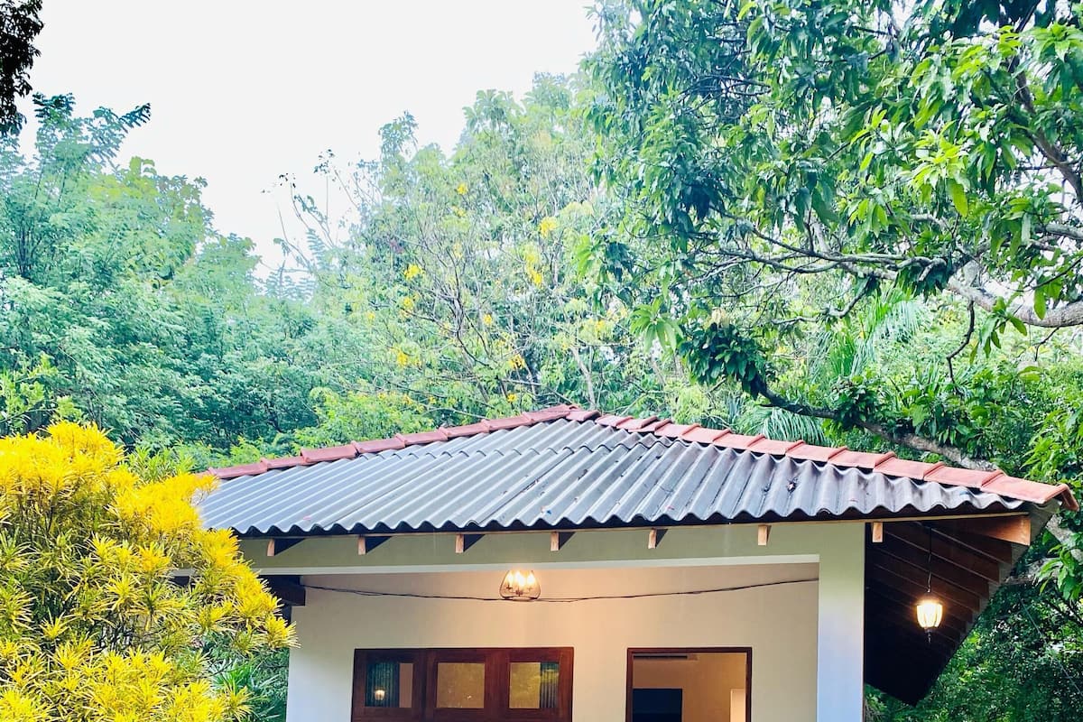 A small house with a tiled roof, a porch with a bench, and a pathway leading to the entrance.