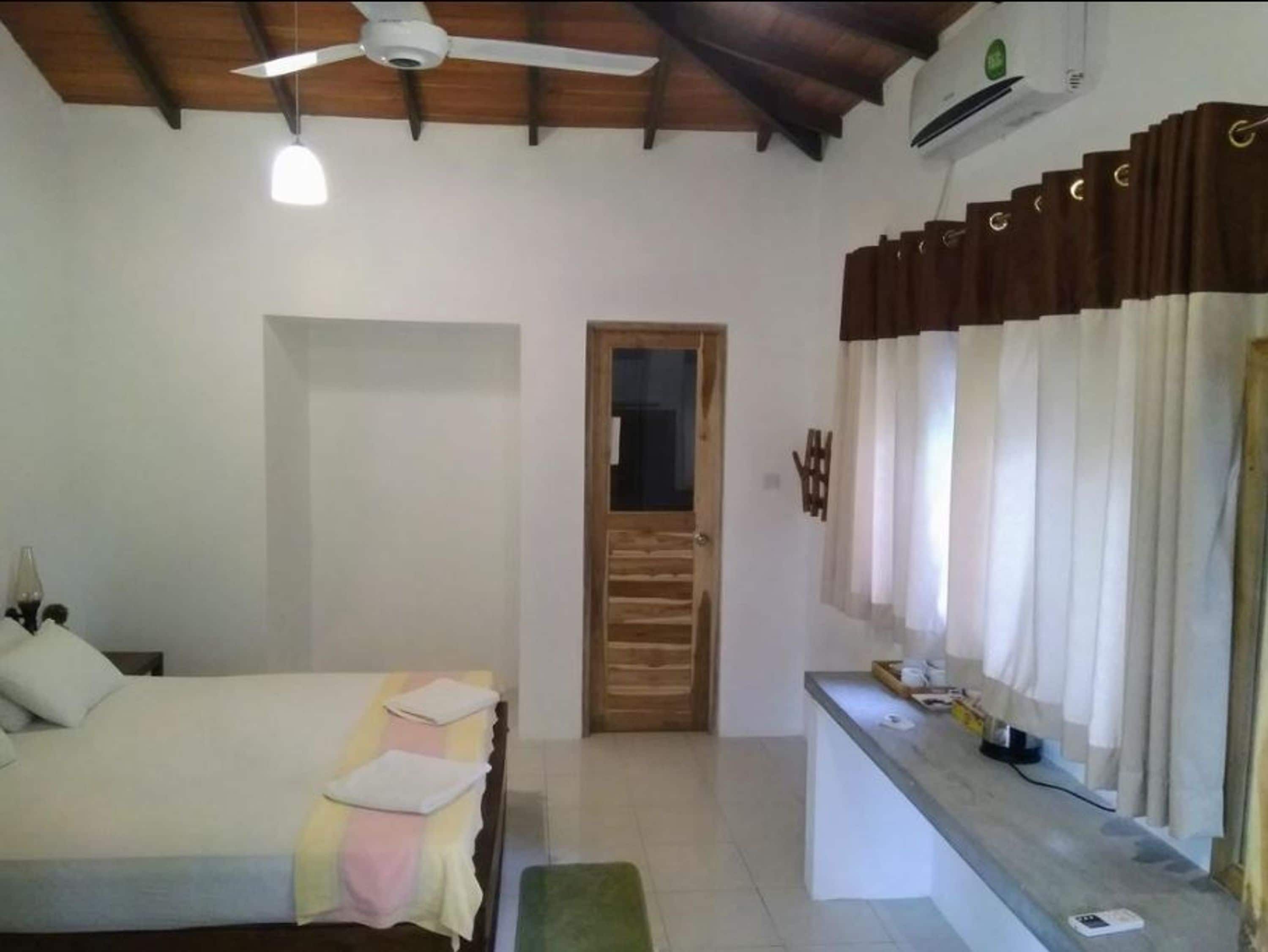 A bedroom with a bed, a desk, a ceiling fan, and a door.