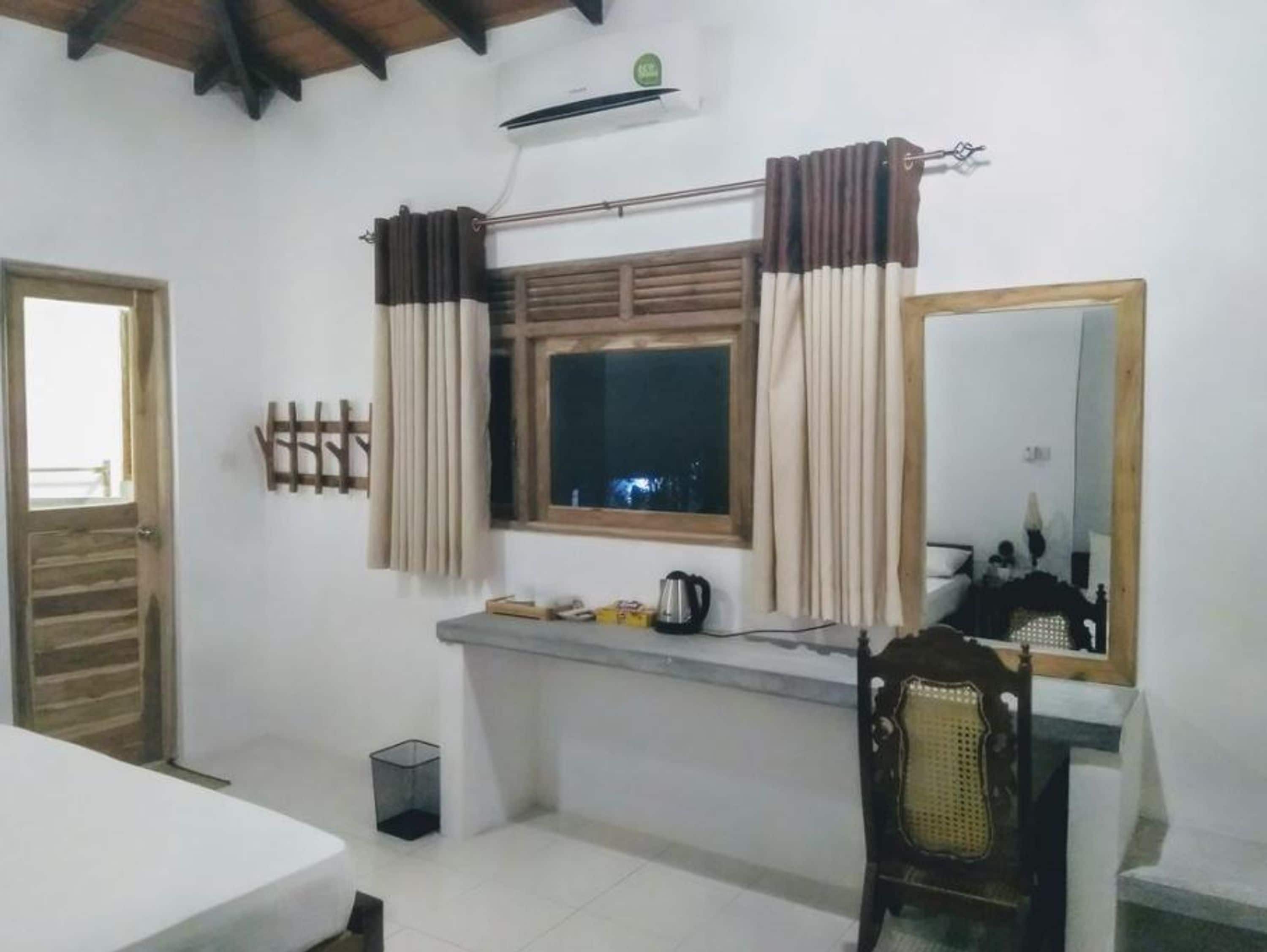 Une petite pièce propre, avec un lit, un bureau et une chaise, une fenêtre avec des rideaux, un miroir et un radiateur.