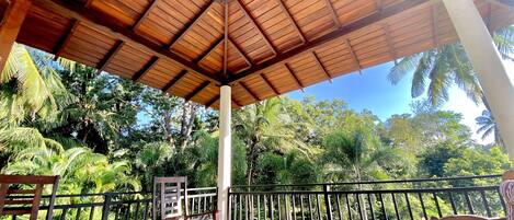 Un espacio al aire libre techado con muebles de madera y vista a árboles tropicales.