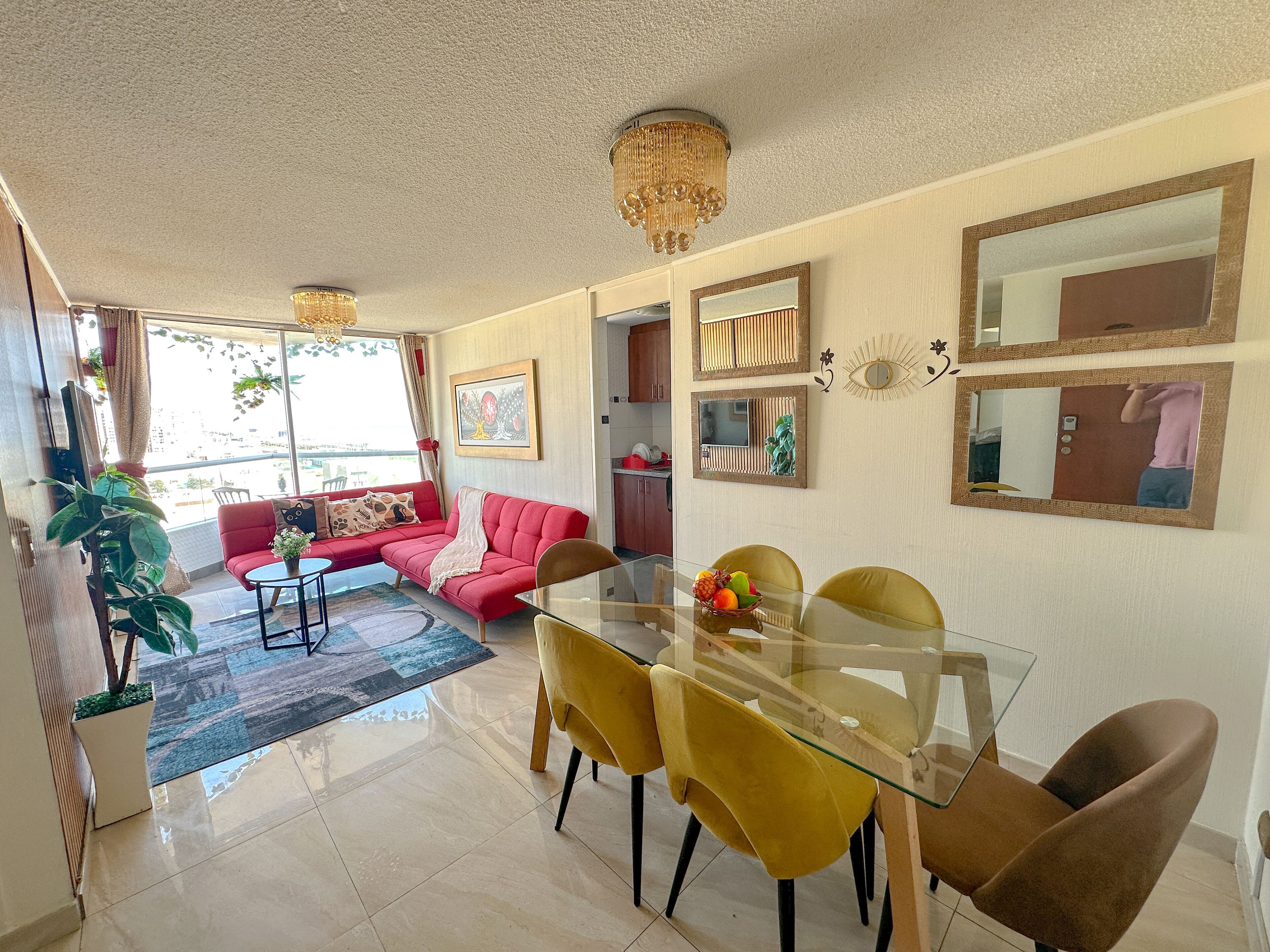 Uma sala de estar moderna com uma mesa de jantar de vidro, cadeiras amarelas, um sofá vermelho e um candelabro.