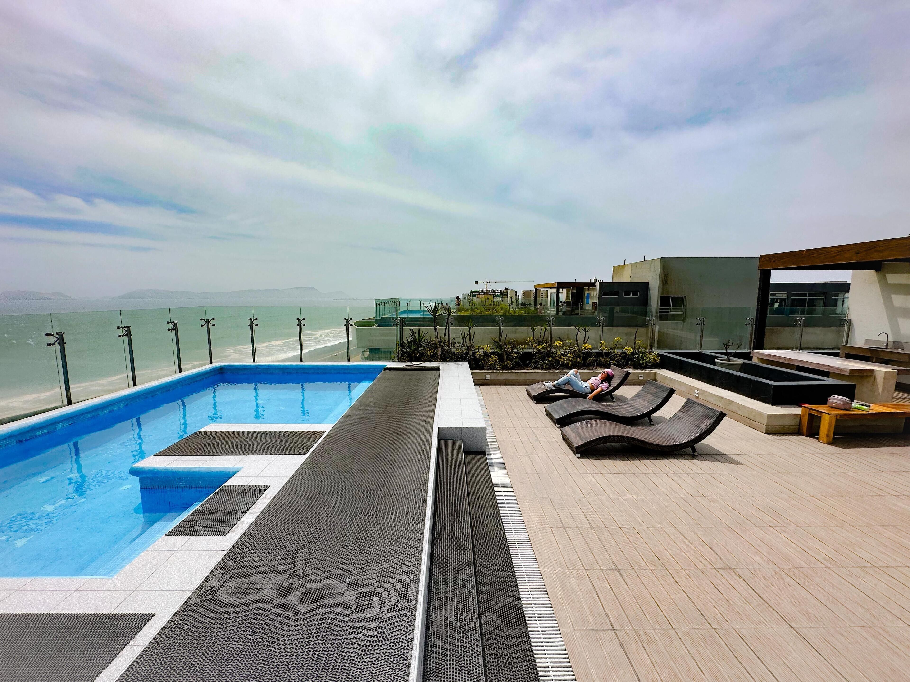 A rooftop pool area with a view of the sea, lounge chairs, and a modern architectural design.