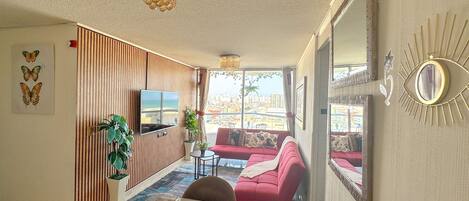 A modern living room with a red sofa, a flat-screen TV, and a large window offering a city view.
