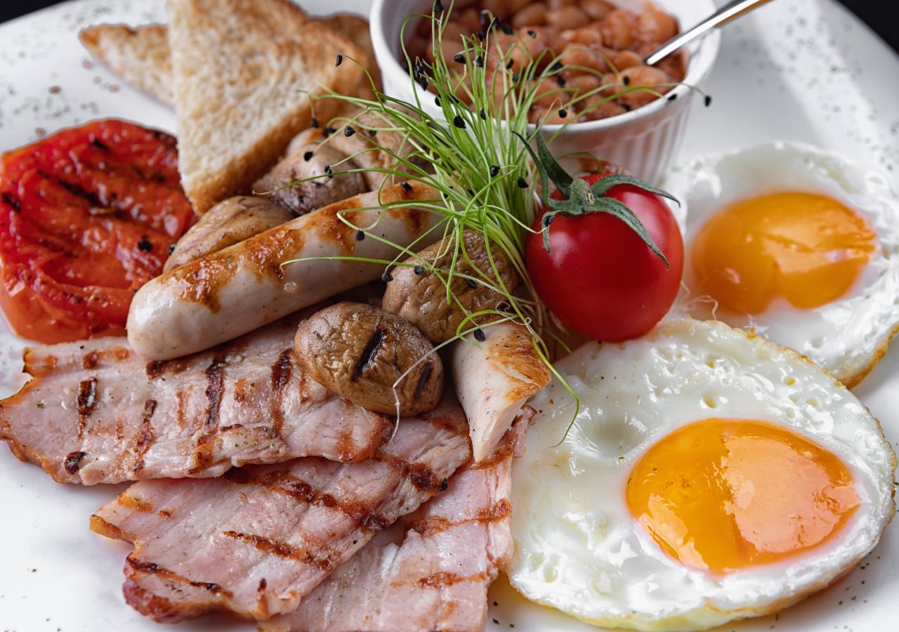 Une assiette de petit-déjeuner comprenant du bacon grillé, des œufs, des champignons, des toasts et une portion de haricots.