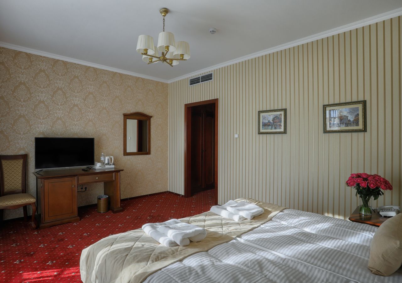 A hotel room with a bed, a desk with a television, a chair, and a door leading to another room.