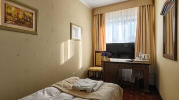Hotellihuone, jossa on sänky, työpöytä tuolilla, televisio ja ikkuna, jossa on verhot.