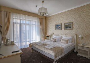 Habitación de hotel con una cama grande, una mesita de noche con lámpara, un escritorio con teléfono y una ventana con cortinas.