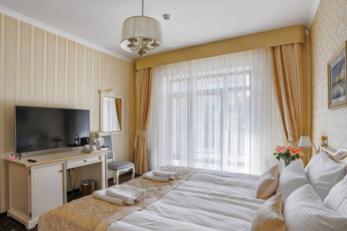 A hotel room with a bed, a desk with a television, a chair, and a window with curtains.