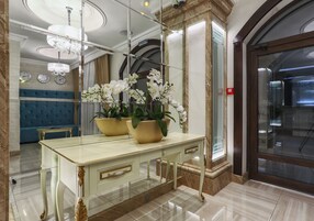 Un baño lujoso con piso de mármol, tocador blanco con detalles dorados y un espejo grande que refleja el ambiente.