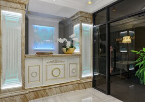 Un vestíbulo con un mostrador de recepción de mármol, una puerta de cristal que da a un restaurante y una planta en maceta.