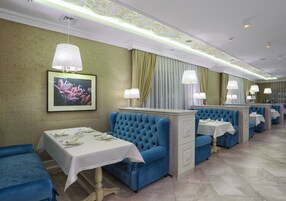 Un restaurante con asientos tapizados en azul, mesas blancas y paredes verdes.