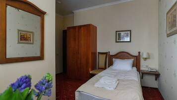 Una habitación de hotel con cama, un armario de madera, una silla, una mesita de noche con lámpara y un cuadro en la pared.