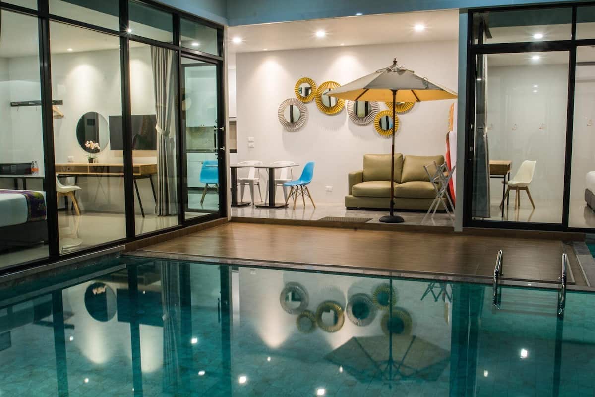 Ein moderner Innenpoolbereich mit Glaswänden, eine Lounge mit Sofa und Sesseln sowie dekorative Spiegel an den Wänden.